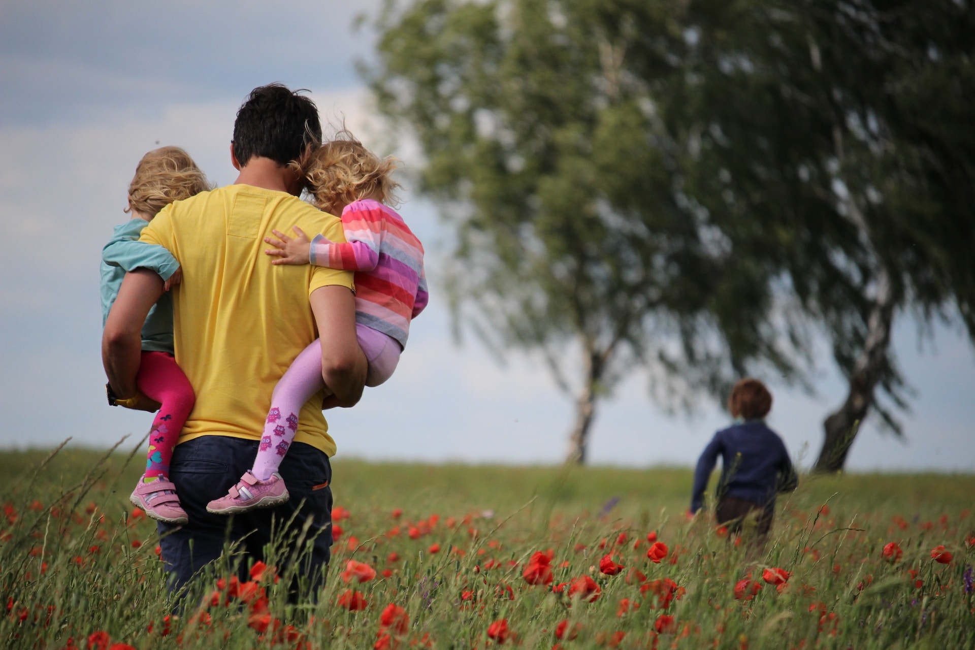 Vater mit Töchtern im Arm auf Feld, Sohn weiter vorn