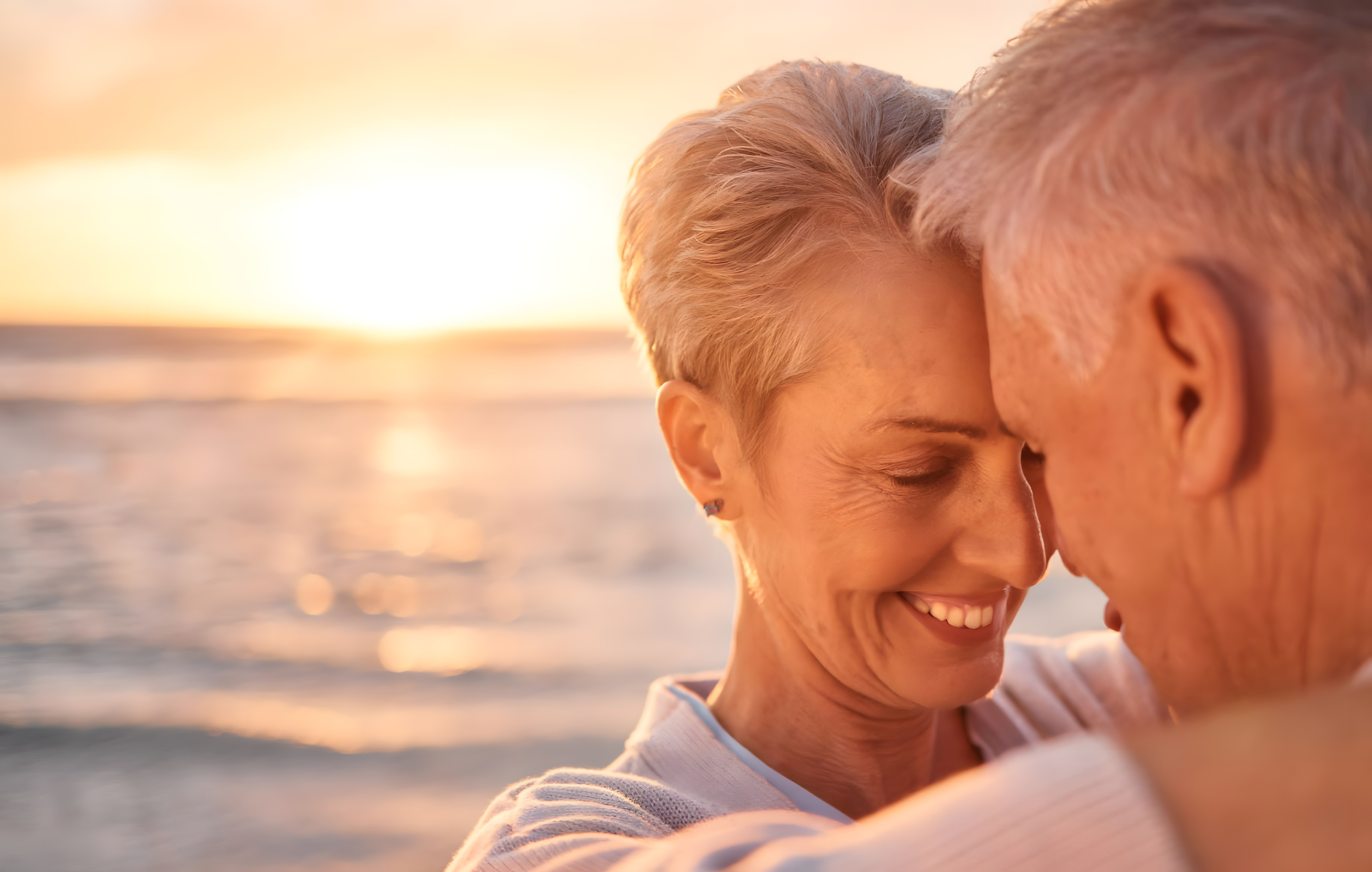 Innige Umarmung eines älteren Paares bei Sonnenuntergang am Meer.